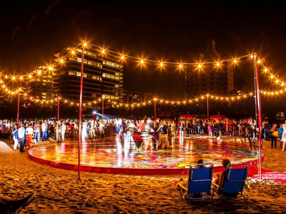 An elevated platform covered in murals on the beach with lights and people rollerskating