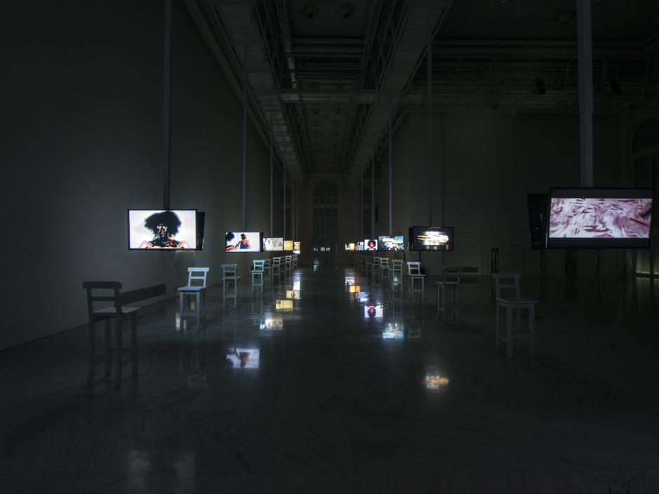 Two rows of televisions with photographs each with a single chair placed in front